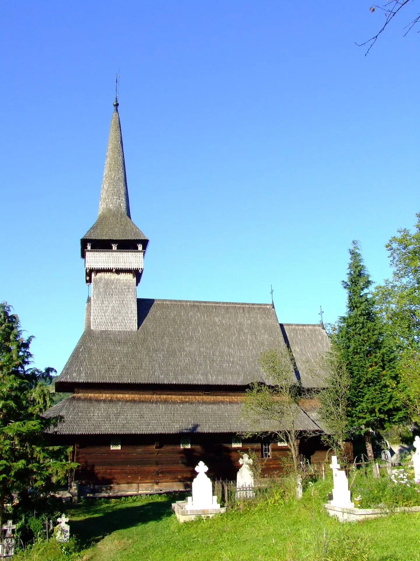 Biserica de lemn din Poienile Izei, cu turn subțire, sub cer senin.