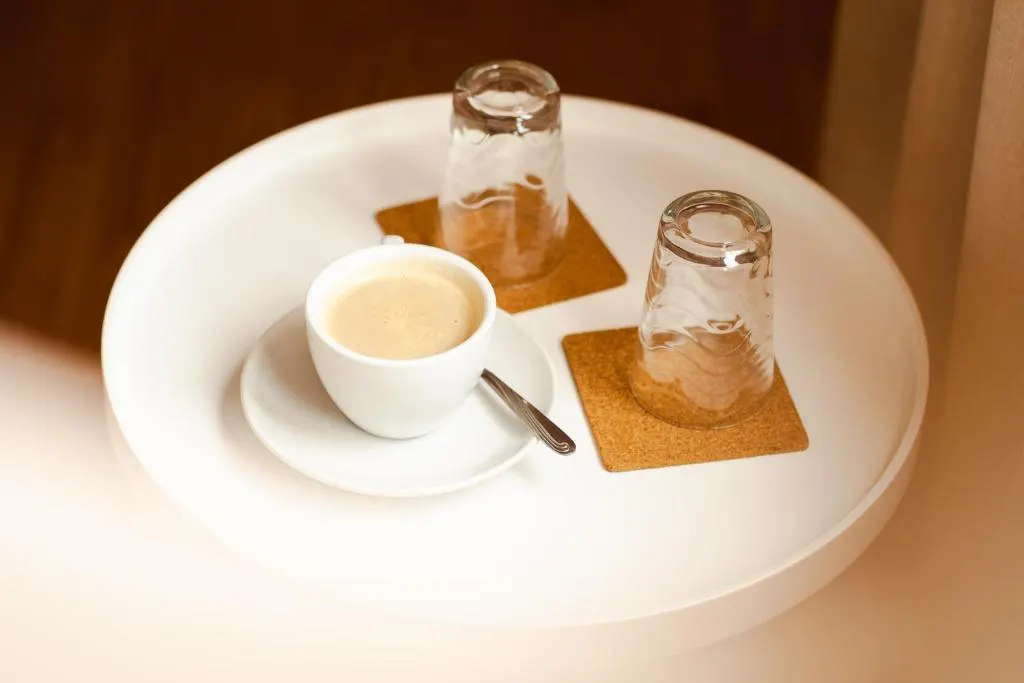 Tavă albă cu o cafea cu lapte și două pahare întoarse pe suporturi de plută.
