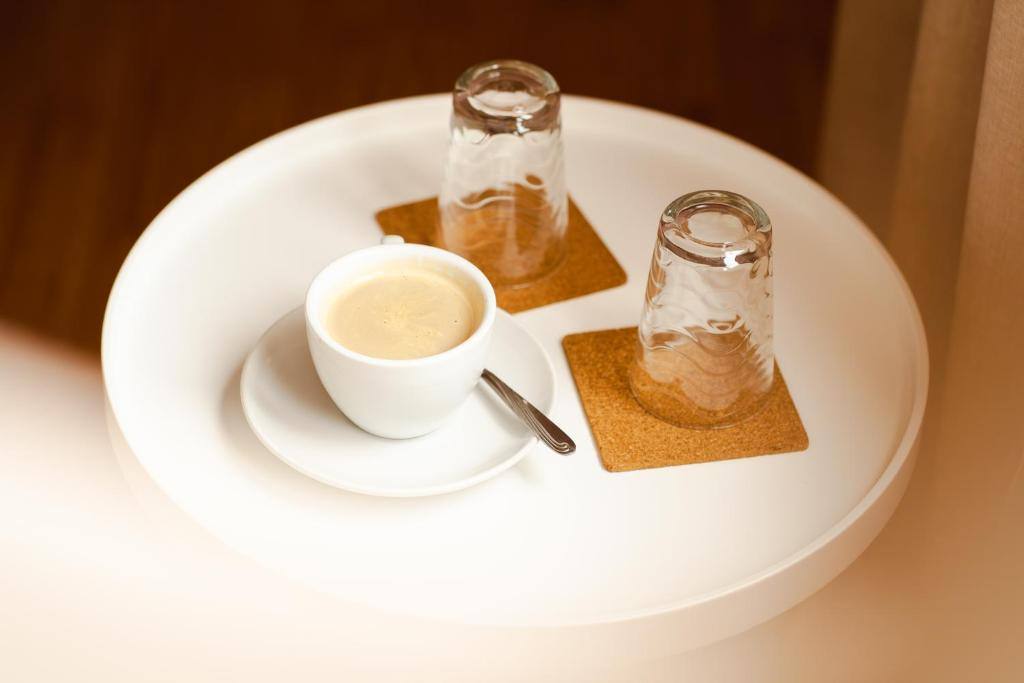 Tavă albă cu o cafea cu lapte și două pahare întoarse pe suporturi de plută.