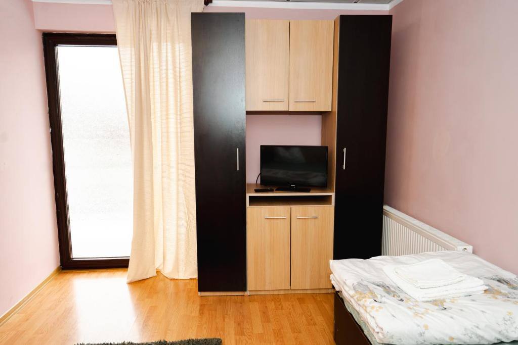 Cameră cu pat single, dulap de haine cu televizor încorporat și ușă spre balcon.