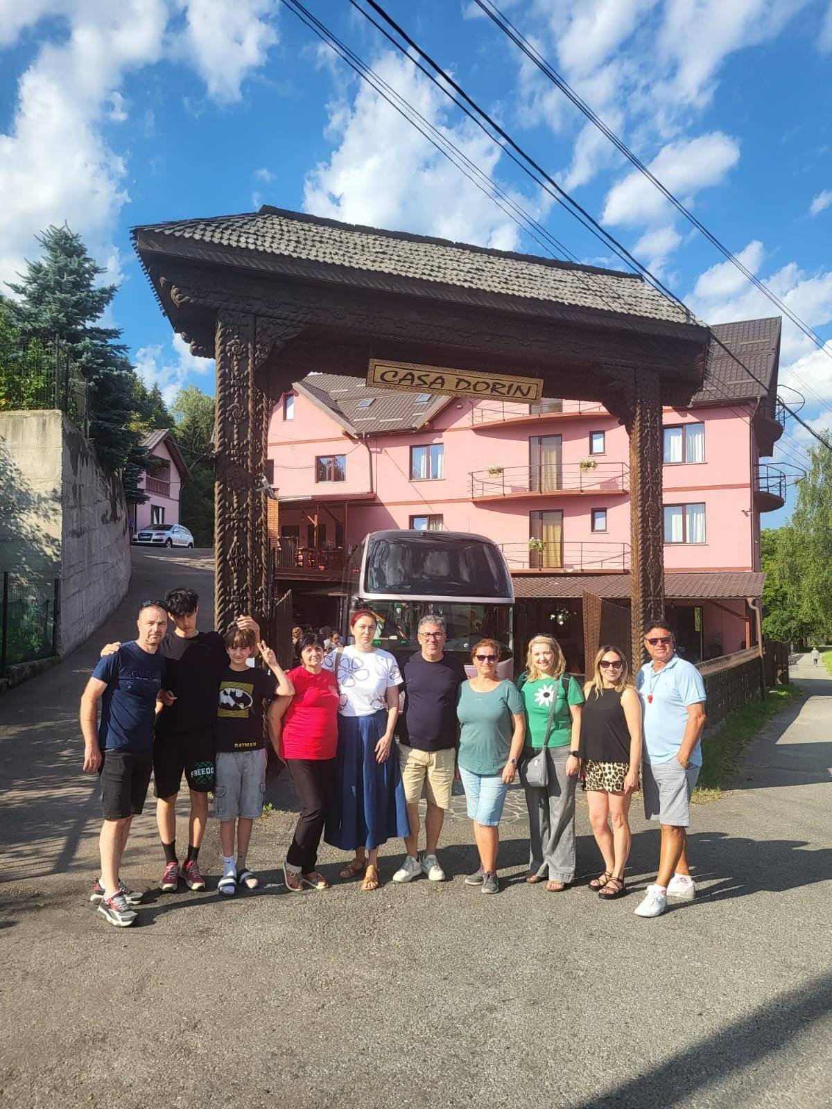 Grup de zece oaspeți în fața pensiunii, cu autocarul în curte.