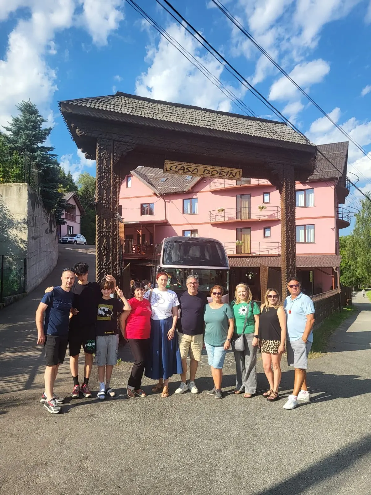 Grup de zece oaspeți în fața pensiunii, cu autocarul în curte.