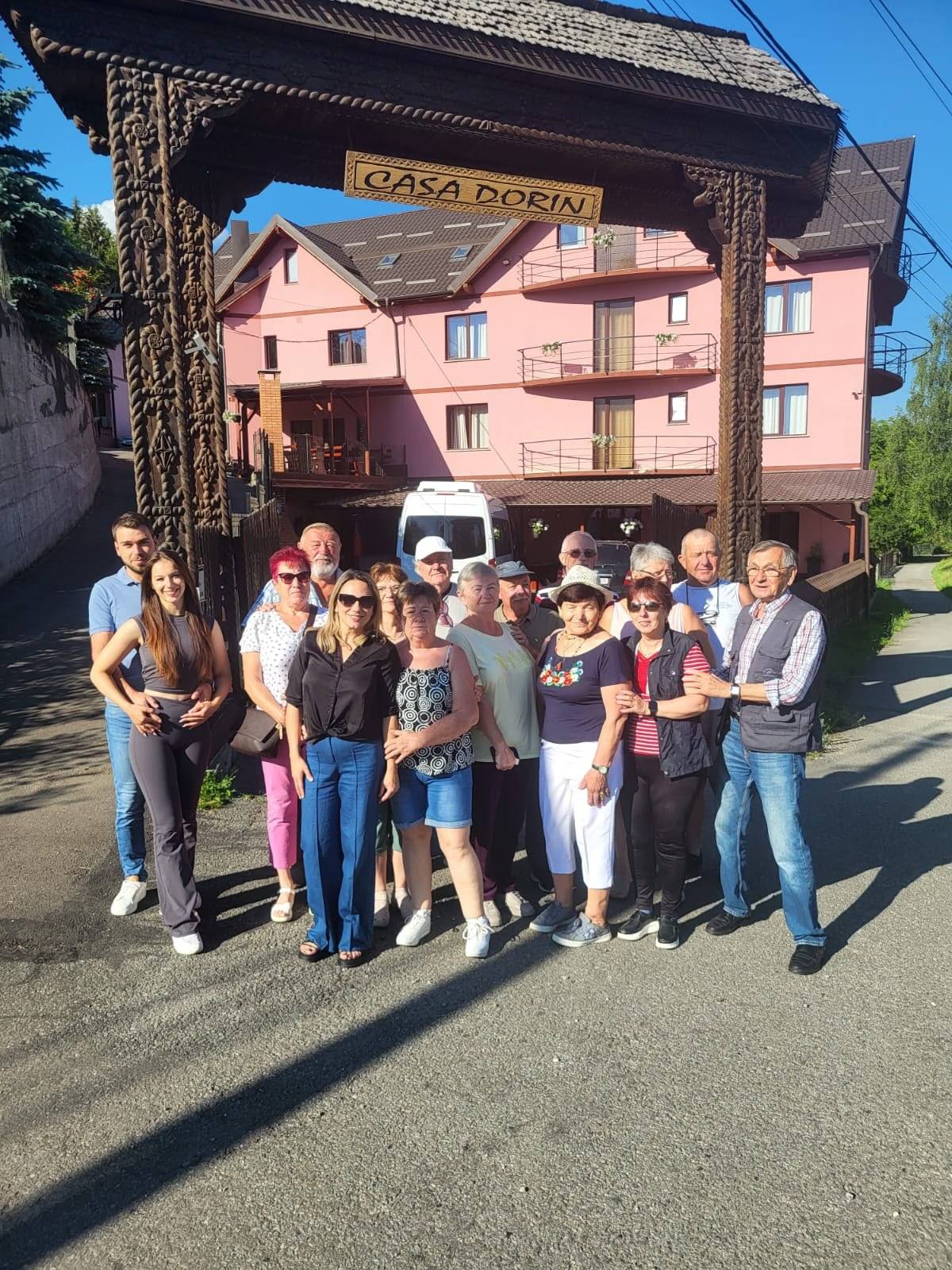 Grup de 16 oaspeți sub poarta pensiunii, cu microbuzul parcat în curte.