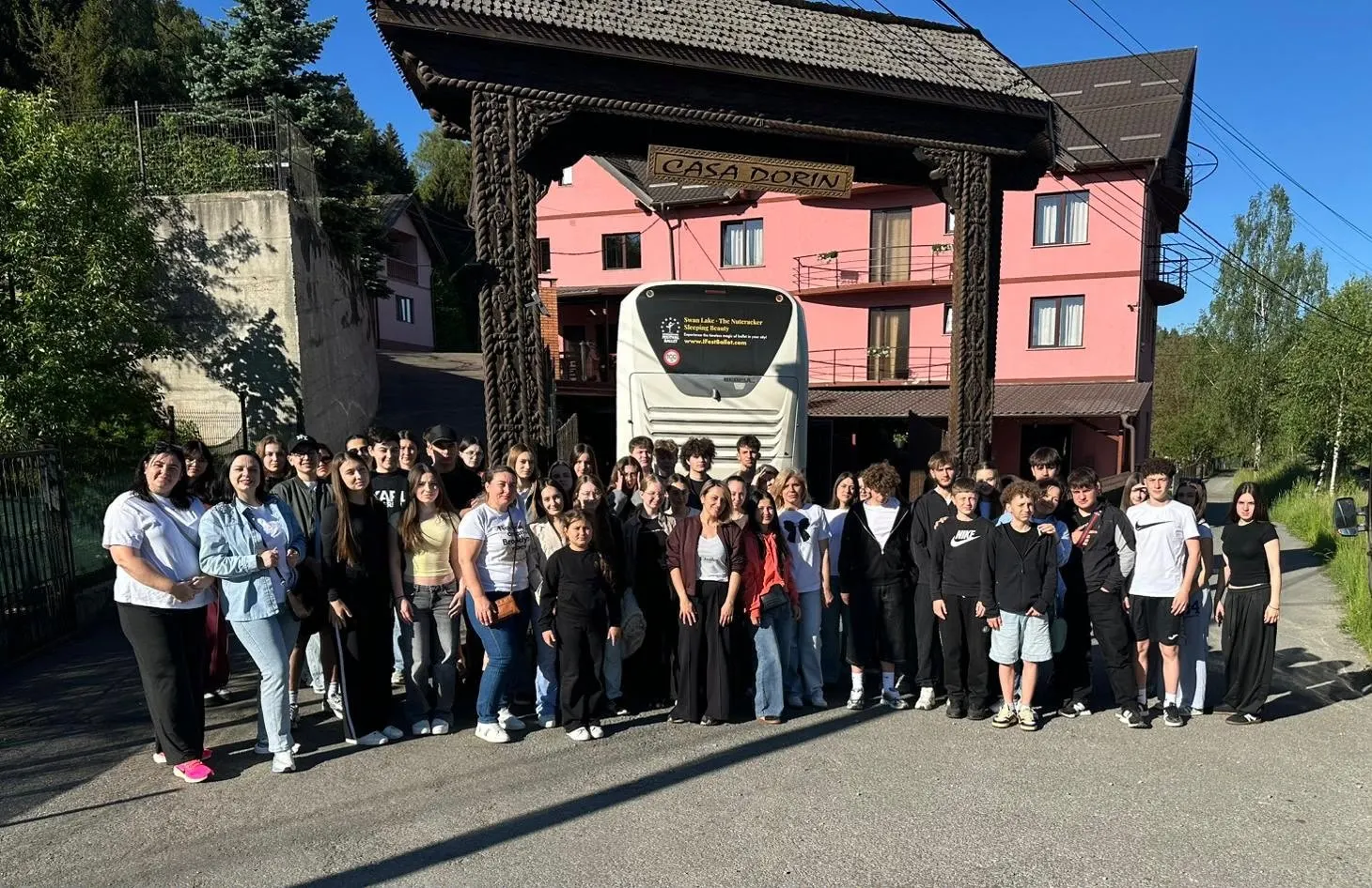 Grup de adolescenți în fața pensiunii, cu autocarul parcat sub poartă.