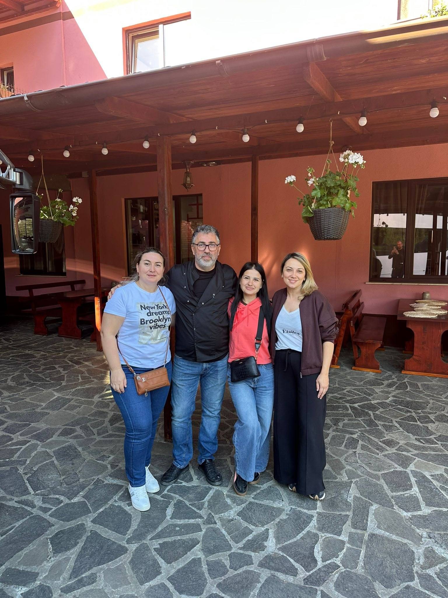 Oaspeți fotografiați în curtea pensiunii, sub terasa acoperită cu ghivece de flori.