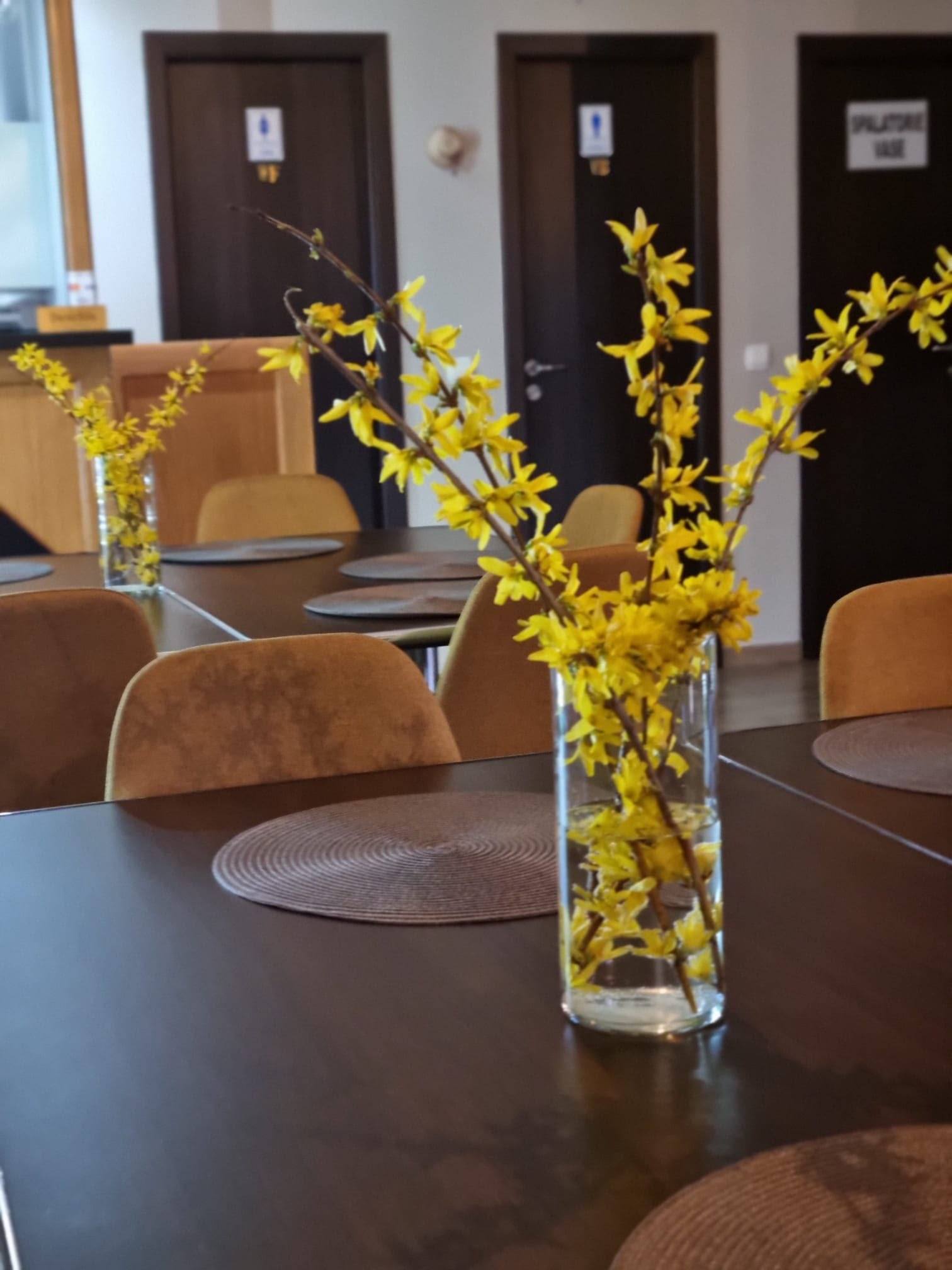 Masă din sala de mese cu o vază de flori galbene de forsiție.