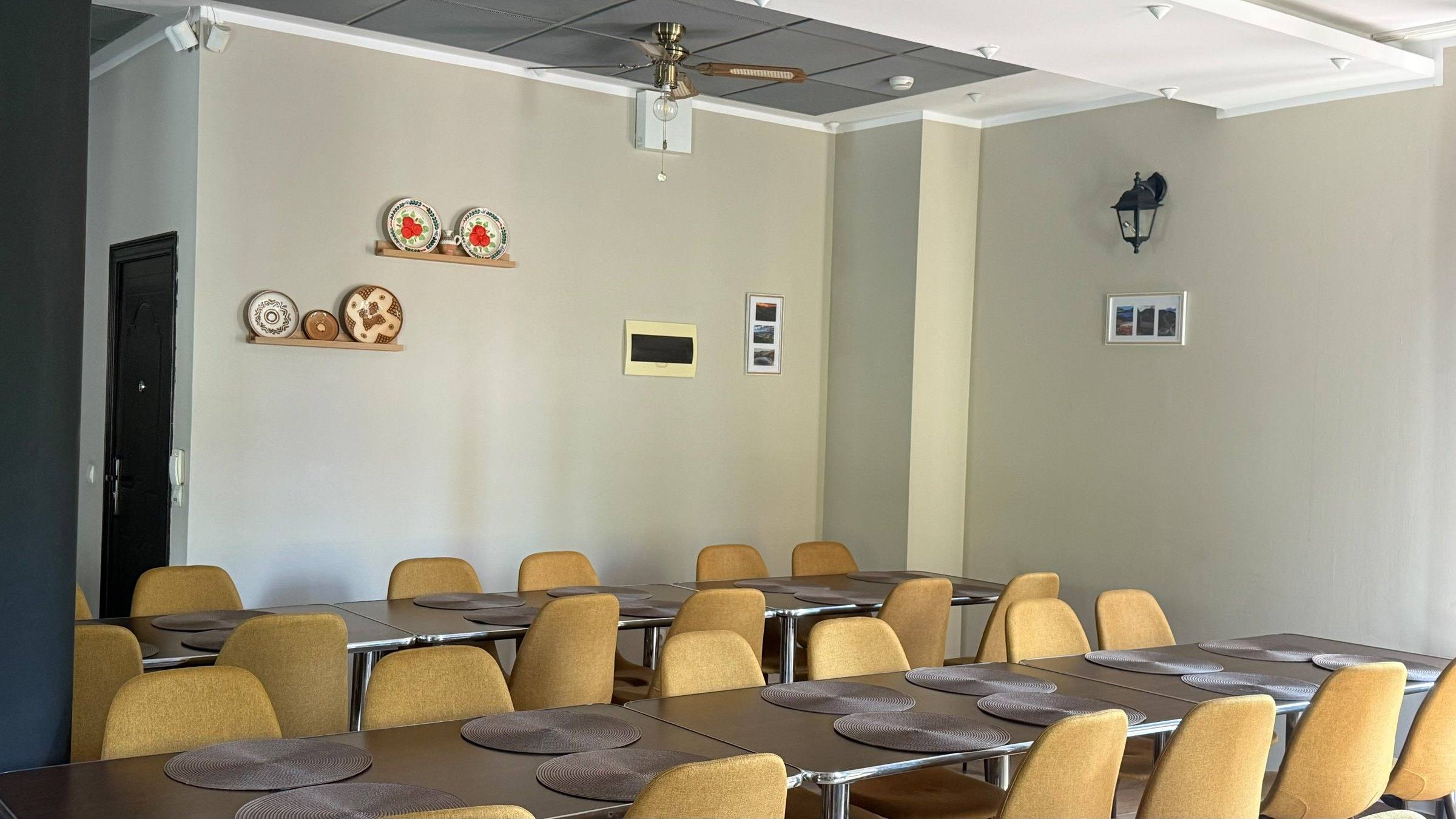 Sala de mese renovată: mese lungi pentru grup, scaune galbene și farfurii de lemn pictate pe perete.