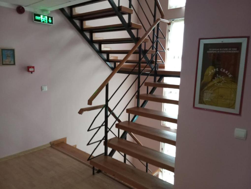 Scara interioară cu trepte de lemn și balustradă metalică, pe holul dintre etaje.