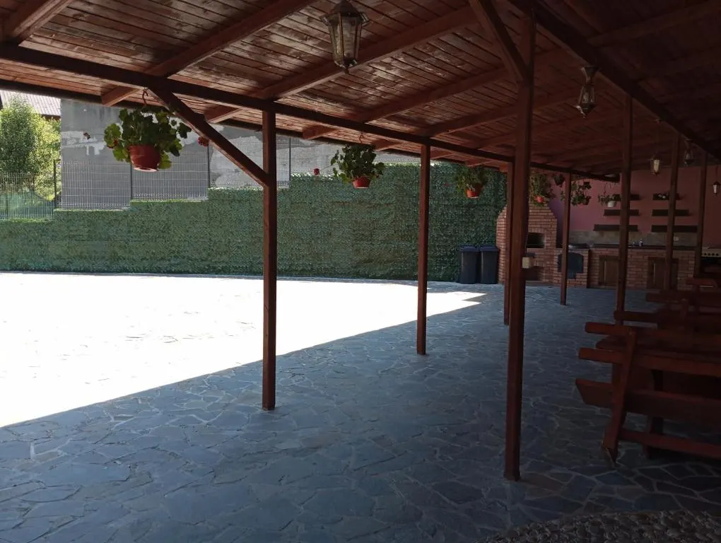 Terasa acoperită cu grinzi de lemn, bănci și mese lungi, cu flori atârnate de stâlpi.